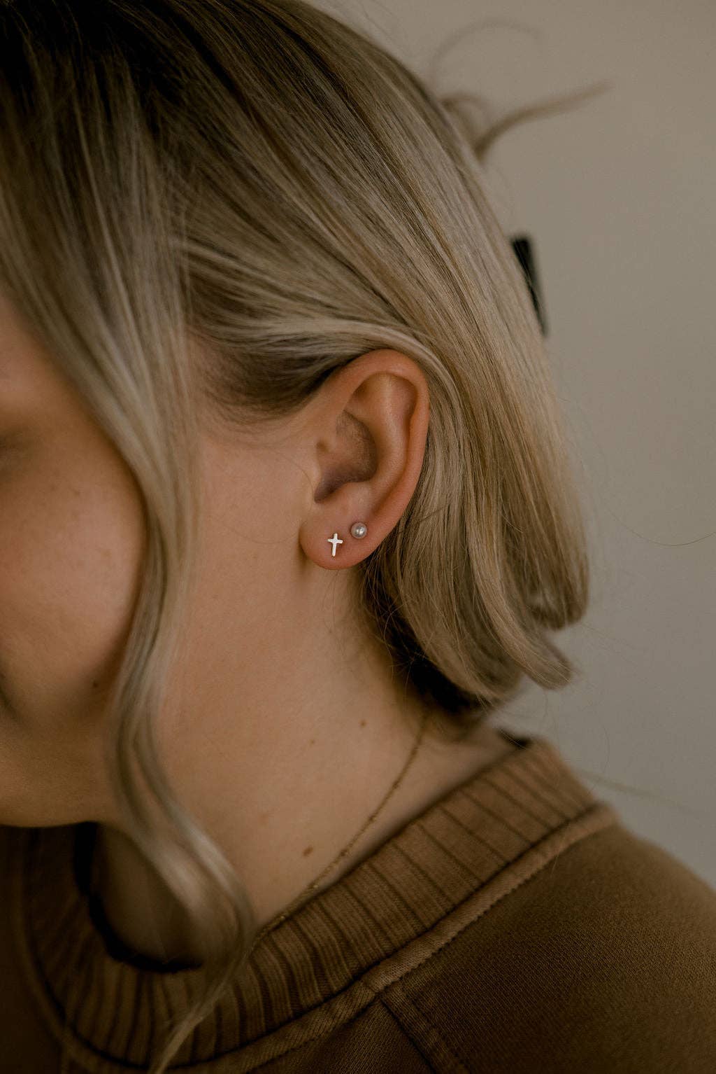 Close-up of a person wearing a cross earring with a neutral background