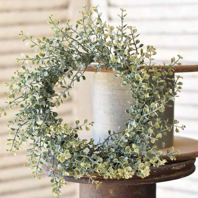 A decorative candle ring with a green floral design, displayed on a wooden spool.