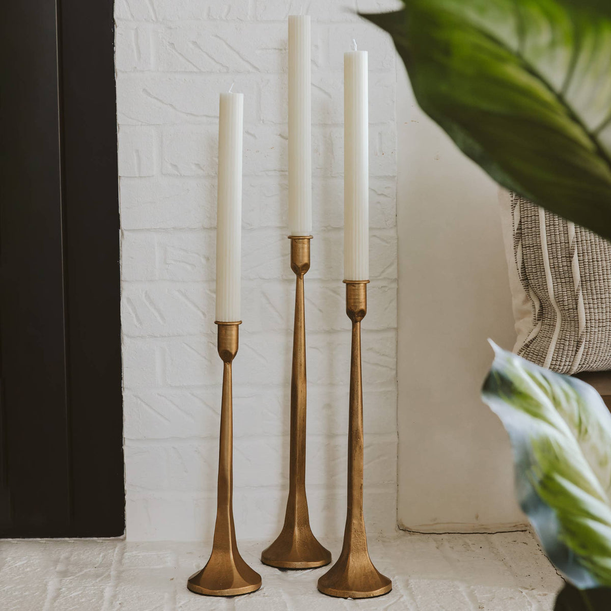A trio of battery taper candles displayed in matte gold candle holders alongside a fireplace