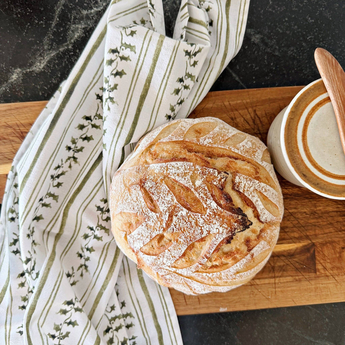Baked goods on a wooden board with a patterned towel and cup in the background
