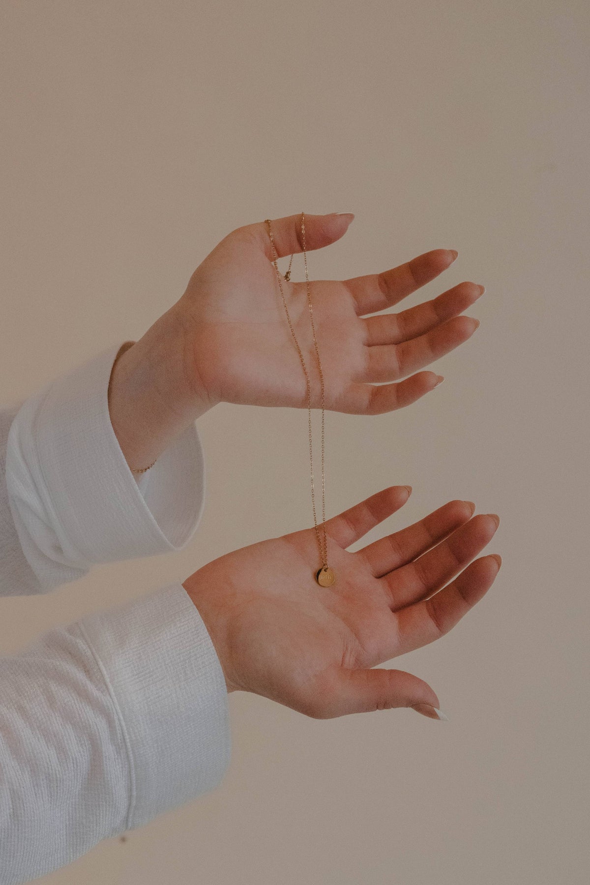 Two hands holding a string with a small pendant necklace, against a plain background