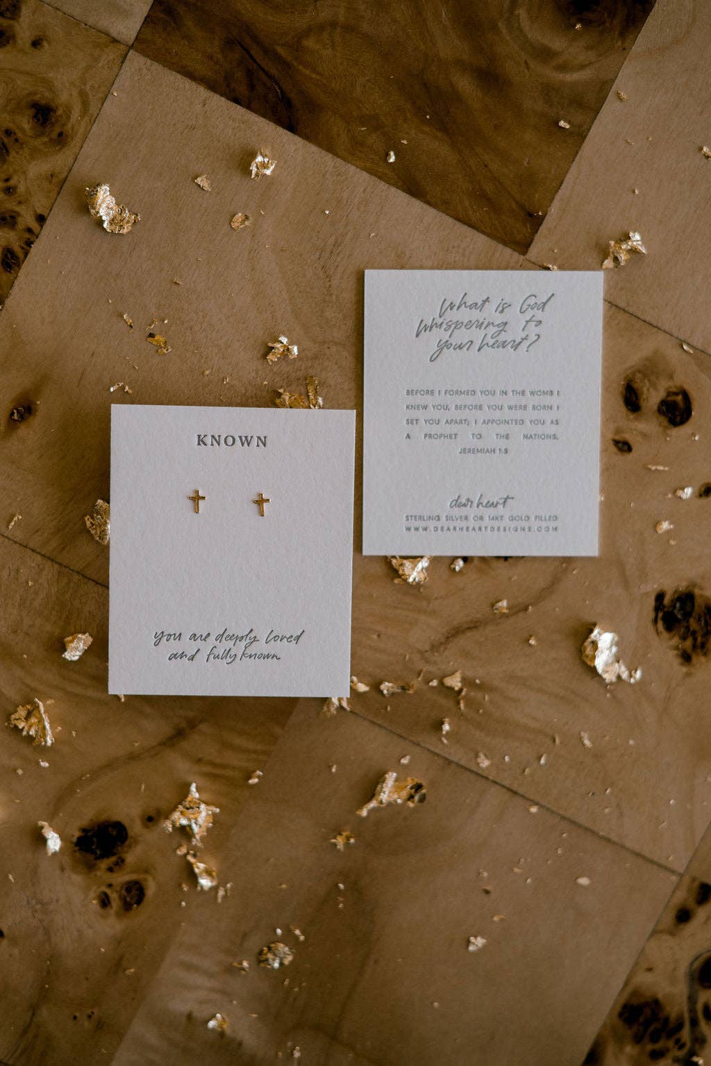 Two cards with text and a cross earring on a textured surface with gold leaf.