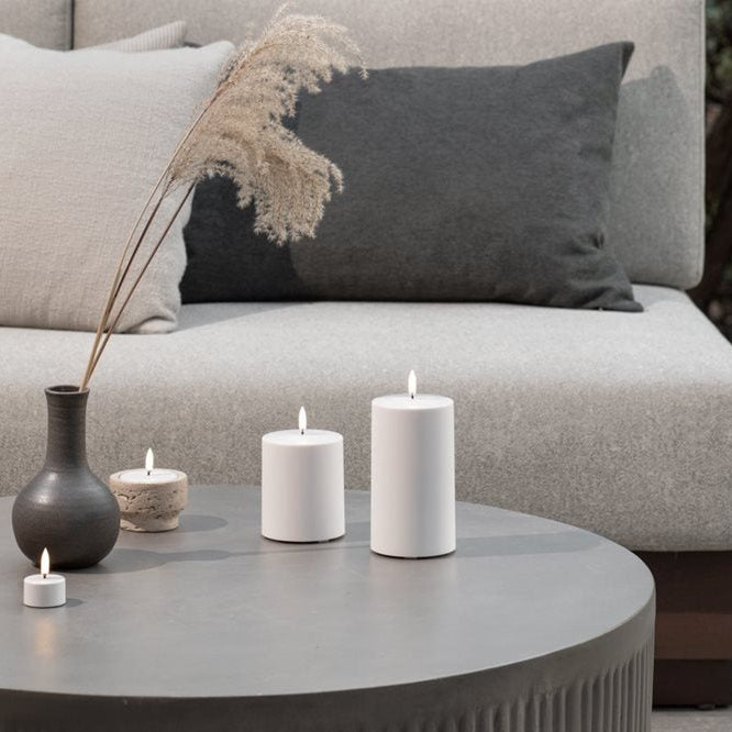 Decorative outdoor setting with candles and vases on a coffee table in front of a sofa.